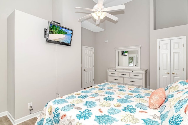 bedroom with baseboards, ceiling fan, wood finished floors, high vaulted ceiling, and a closet