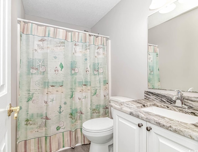 full bathroom with a textured ceiling, toilet, and vanity