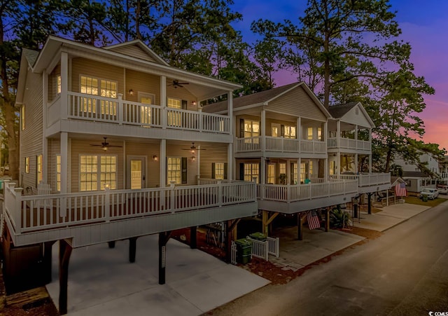 back of house at dusk featuring a balcony, ceiling fan, cooling unit, and concrete driveway