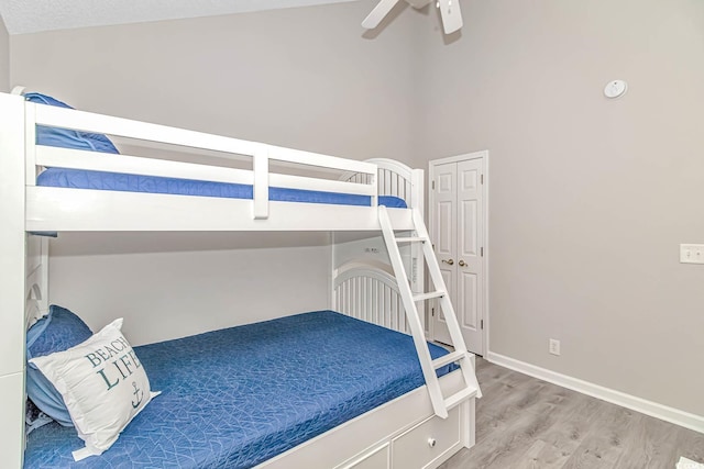 bedroom with a towering ceiling, a ceiling fan, baseboards, and wood finished floors