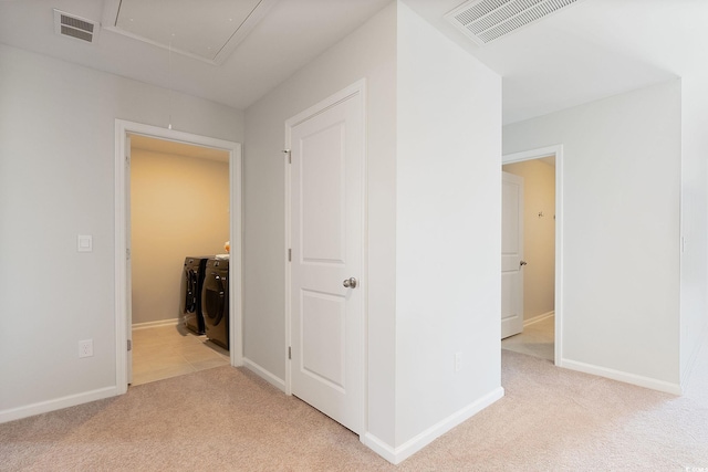 hallway with attic access, independent washer and dryer, light colored carpet, and visible vents