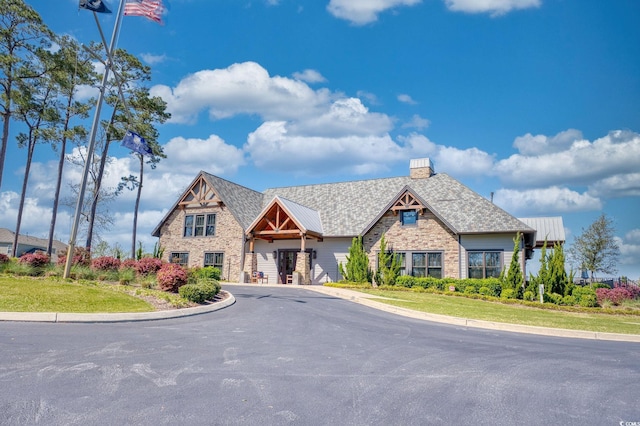 view of front of house featuring stone siding, a chimney, and driveway