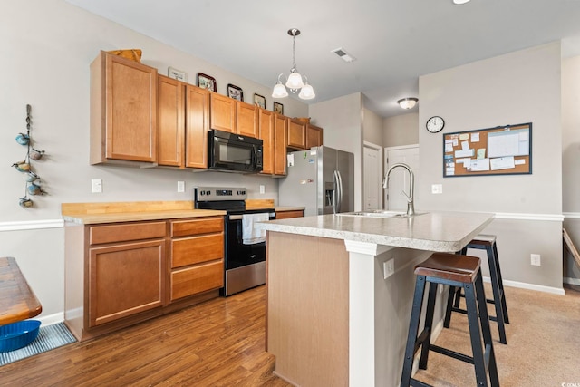 kitchen with visible vents, a center island with sink, a sink, stainless steel appliances, and light countertops