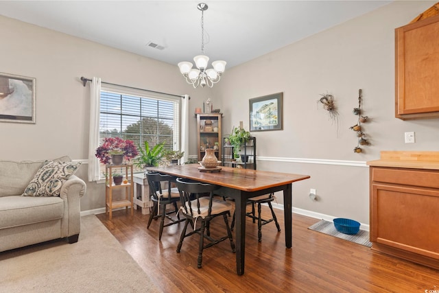 dining room featuring a notable chandelier, baseboards, visible vents, and wood finished floors