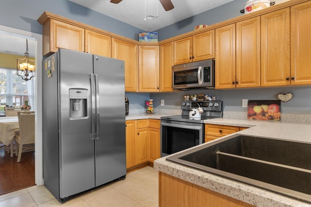 kitchen featuring sink, a textured ceiling, light tile patterned floors, appliances with stainless steel finishes, and ceiling fan with notable chandelier