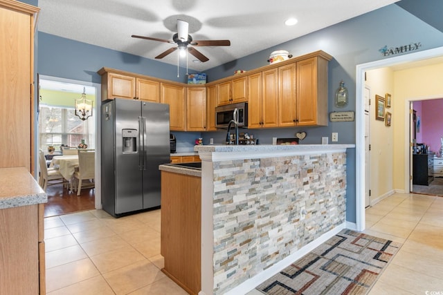 kitchen with light tile patterned flooring, appliances with stainless steel finishes, ceiling fan with notable chandelier, and kitchen peninsula