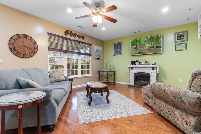 living room featuring a fireplace, wood-type flooring, and ceiling fan