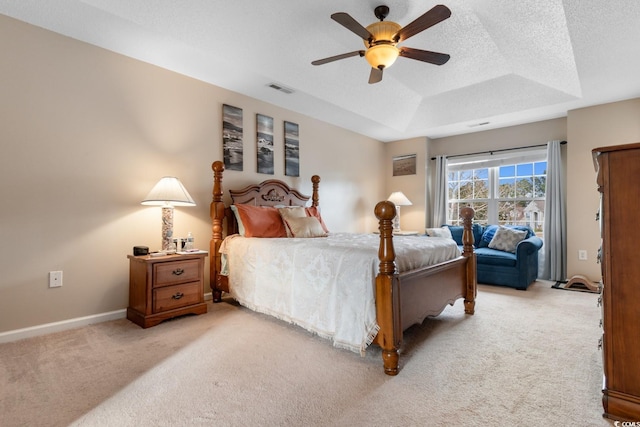 bedroom with a raised ceiling, ceiling fan, light colored carpet, and a textured ceiling