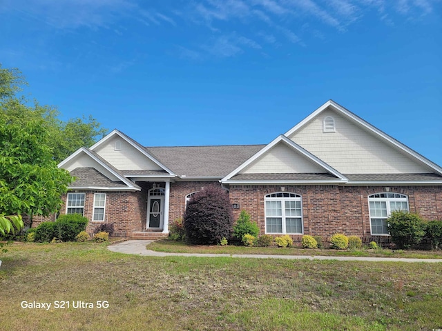 ranch-style home featuring brick siding, a front yard, and a shingled roof