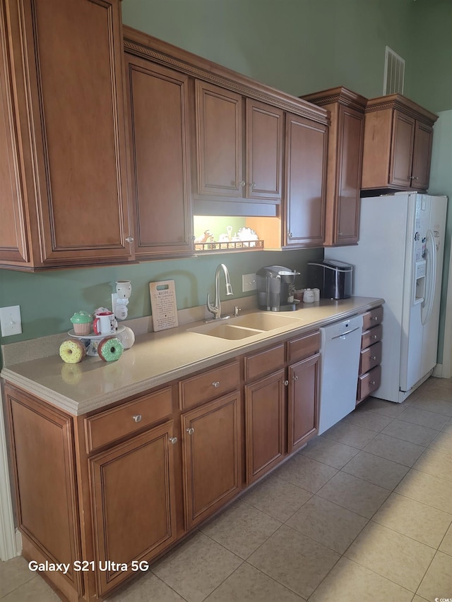 kitchen featuring white appliances, a sink, light countertops, light tile patterned floors, and brown cabinetry