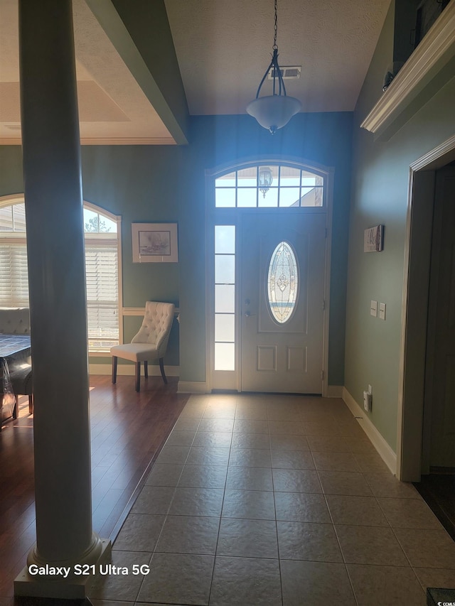 foyer entrance featuring baseboards, visible vents, and dark tile patterned flooring