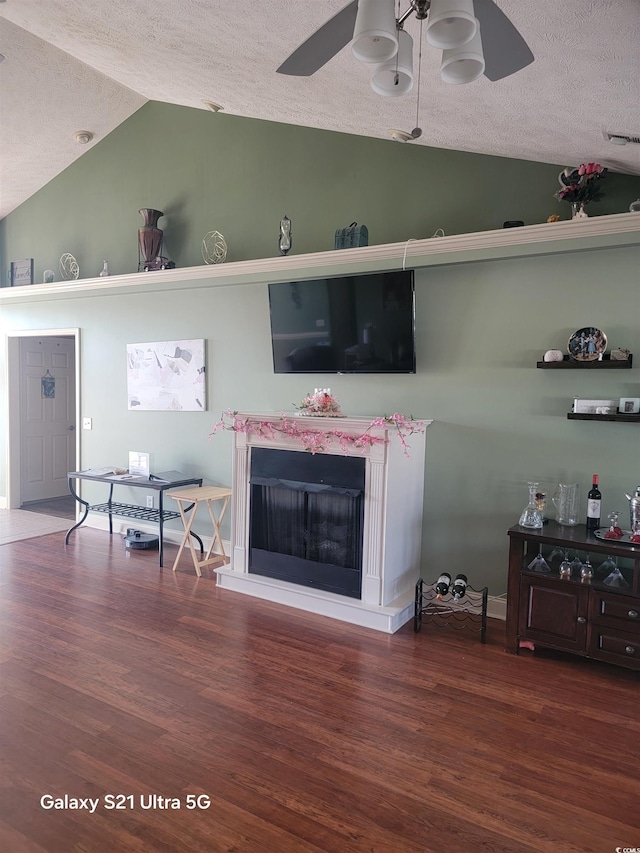 living room featuring lofted ceiling, ceiling fan, a textured ceiling, wood finished floors, and a fireplace
