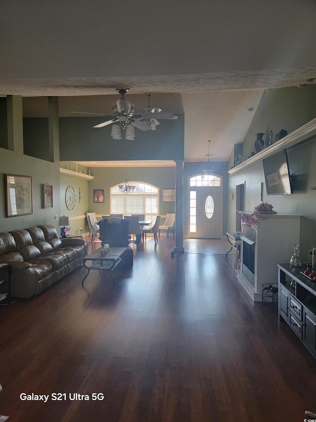 living area featuring dark wood-style flooring, ceiling fan, a chandelier, and vaulted ceiling