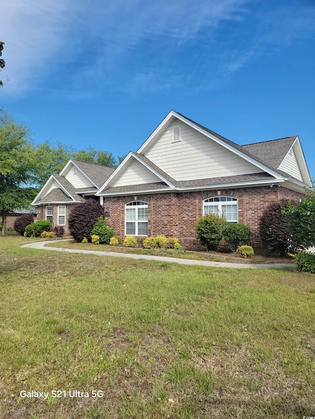 view of front of property with a front lawn, brick siding, and a shingled roof