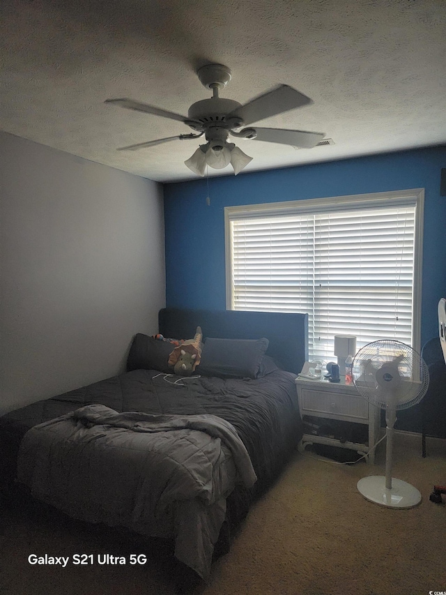 carpeted bedroom featuring a ceiling fan and a textured ceiling