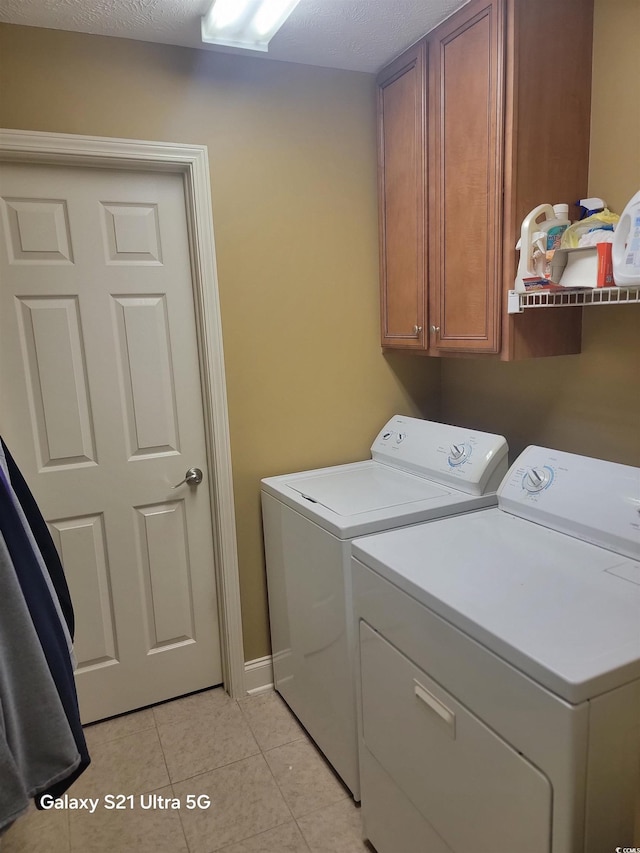 washroom featuring light tile patterned floors, cabinet space, washing machine and dryer, a textured ceiling, and baseboards