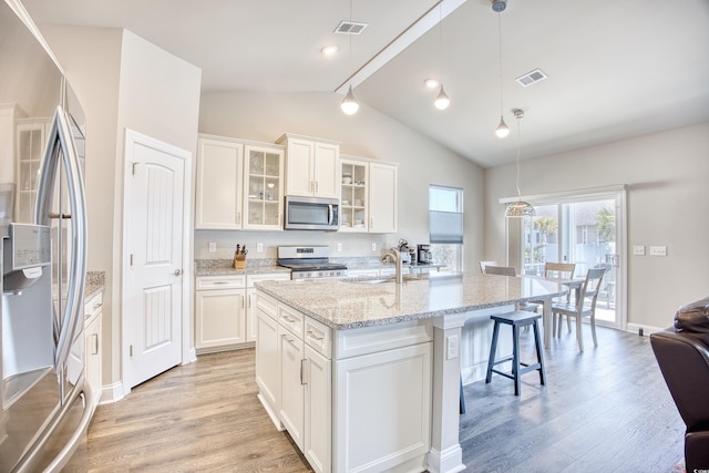 kitchen with pendant lighting, stainless steel appliances, a kitchen island with sink, and white cabinets