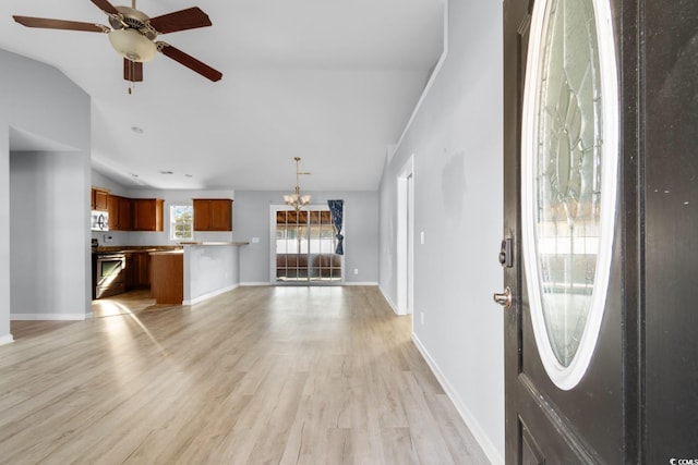 entryway with ceiling fan with notable chandelier, vaulted ceiling, and light wood-type flooring