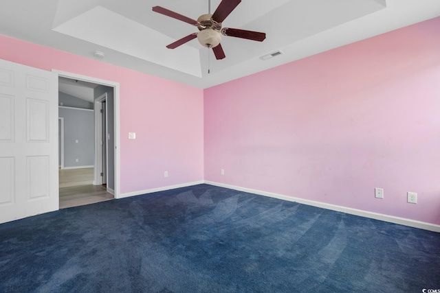 unfurnished bedroom with a tray ceiling, ceiling fan, and dark colored carpet