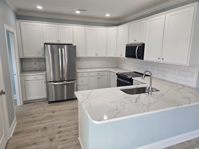 kitchen featuring a peninsula, a sink, white cabinets, freestanding refrigerator, and light stone countertops