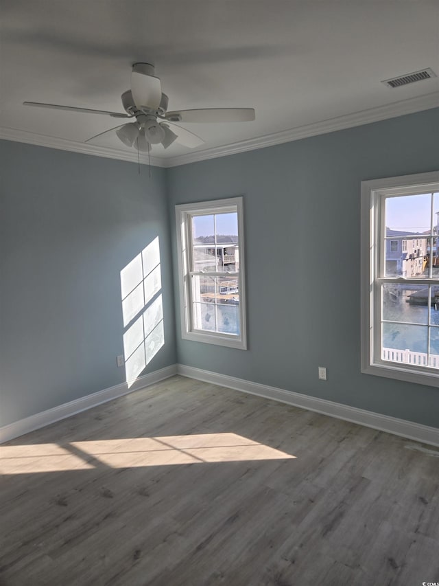 empty room featuring baseboards, visible vents, a ceiling fan, wood finished floors, and crown molding