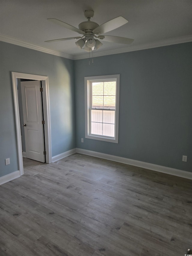 empty room with a ceiling fan, baseboards, crown molding, and wood finished floors