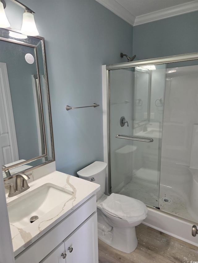 bathroom featuring toilet, wood finished floors, vanity, a stall shower, and crown molding