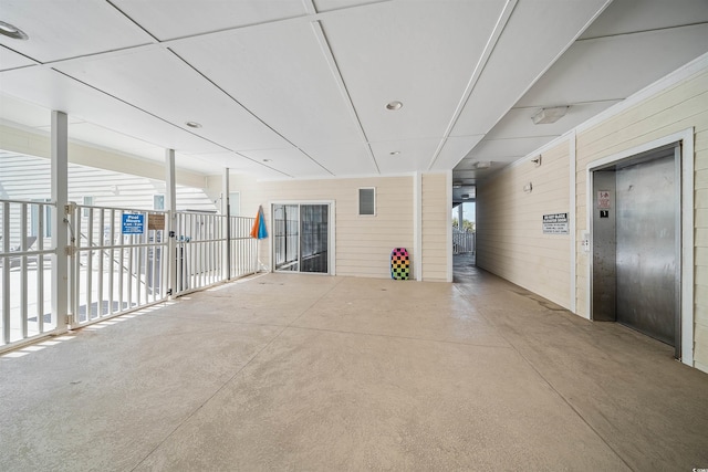 empty room featuring wood walls, concrete floors, and elevator