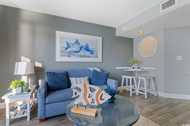 living room with visible vents, baseboards, a textured ceiling, and wood finished floors