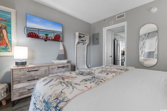 bedroom with electric panel, wood finished floors, visible vents, and freestanding refrigerator