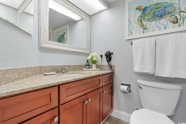 bathroom featuring vanity, toilet, a textured wall, and baseboards