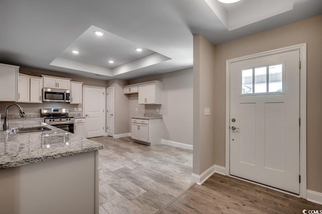 kitchen with sink, appliances with stainless steel finishes, white cabinetry, a tray ceiling, and light stone countertops