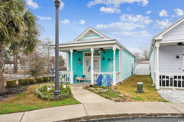 shotgun-style home featuring a ceiling fan, fence, covered porch, a front yard, and metal roof