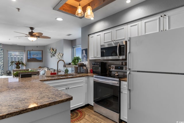 kitchen featuring light wood finished floors, appliances with stainless steel finishes, white cabinetry, a sink, and a peninsula