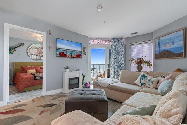 living room with wood finished floors, a glass covered fireplace, visible vents, and baseboards