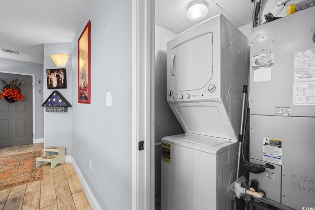 washroom featuring stacked washer / drying machine, heating unit, and light hardwood / wood-style flooring