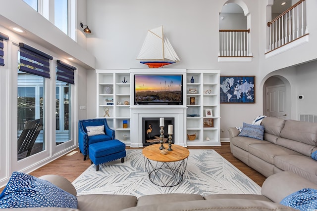 living room with built in shelves, wood-type flooring, and a towering ceiling