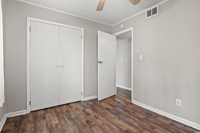 unfurnished bedroom featuring dark wood-type flooring, a textured ceiling, ornamental molding, a closet, and ceiling fan