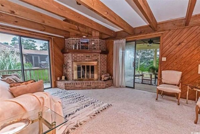 carpeted living room featuring plenty of natural light, beam ceiling, a brick fireplace, and wood walls