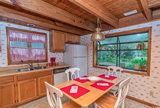 kitchen with sink, beamed ceiling, stainless steel dishwasher, white fridge, and pendant lighting