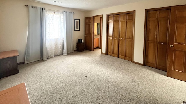 unfurnished bedroom featuring multiple closets, light colored carpet, and a textured ceiling