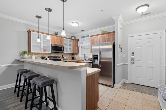 kitchen with a breakfast bar, backsplash, stainless steel appliances, decorative light fixtures, and kitchen peninsula