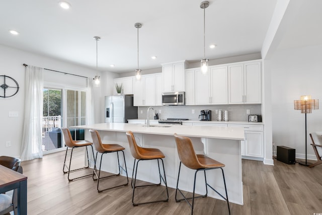 kitchen featuring stainless steel appliances, pendant lighting, a center island with sink, and decorative backsplash