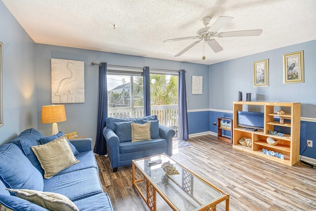 living room featuring a textured ceiling, wood finished floors, a ceiling fan, and baseboards