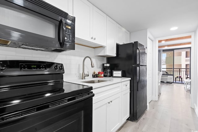 kitchen featuring sink, white cabinetry, black appliances, decorative backsplash, and light wood-type flooring