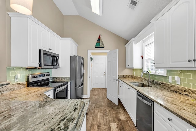 kitchen featuring sink, appliances with stainless steel finishes, light stone countertops, white cabinets, and vaulted ceiling