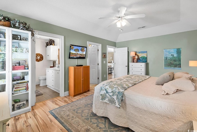 bedroom featuring vaulted ceiling, ensuite bathroom, light wood-type flooring, ceiling fan, and a textured ceiling