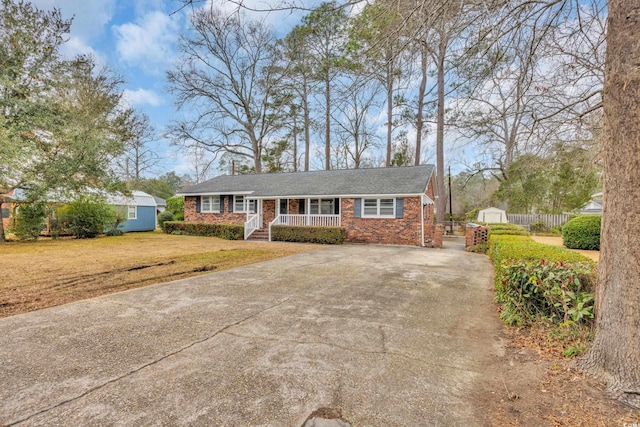 single story home featuring a front lawn, covered porch, and a shed