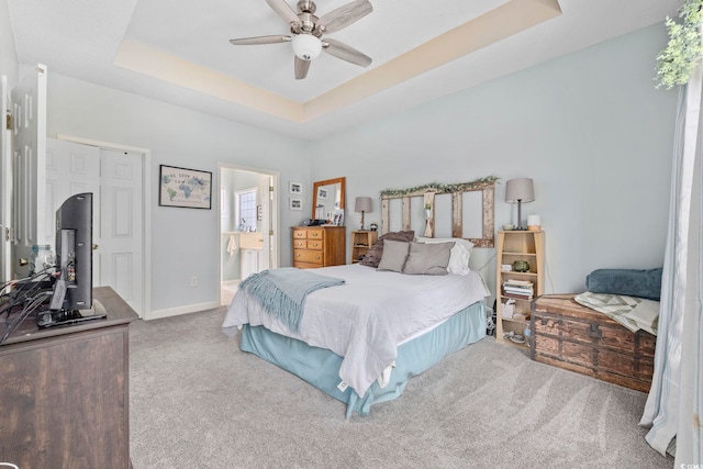 carpeted bedroom featuring ceiling fan, ensuite bath, and a tray ceiling