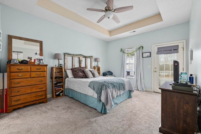 bedroom with ceiling fan, carpet flooring, a tray ceiling, a textured ceiling, and access to outside